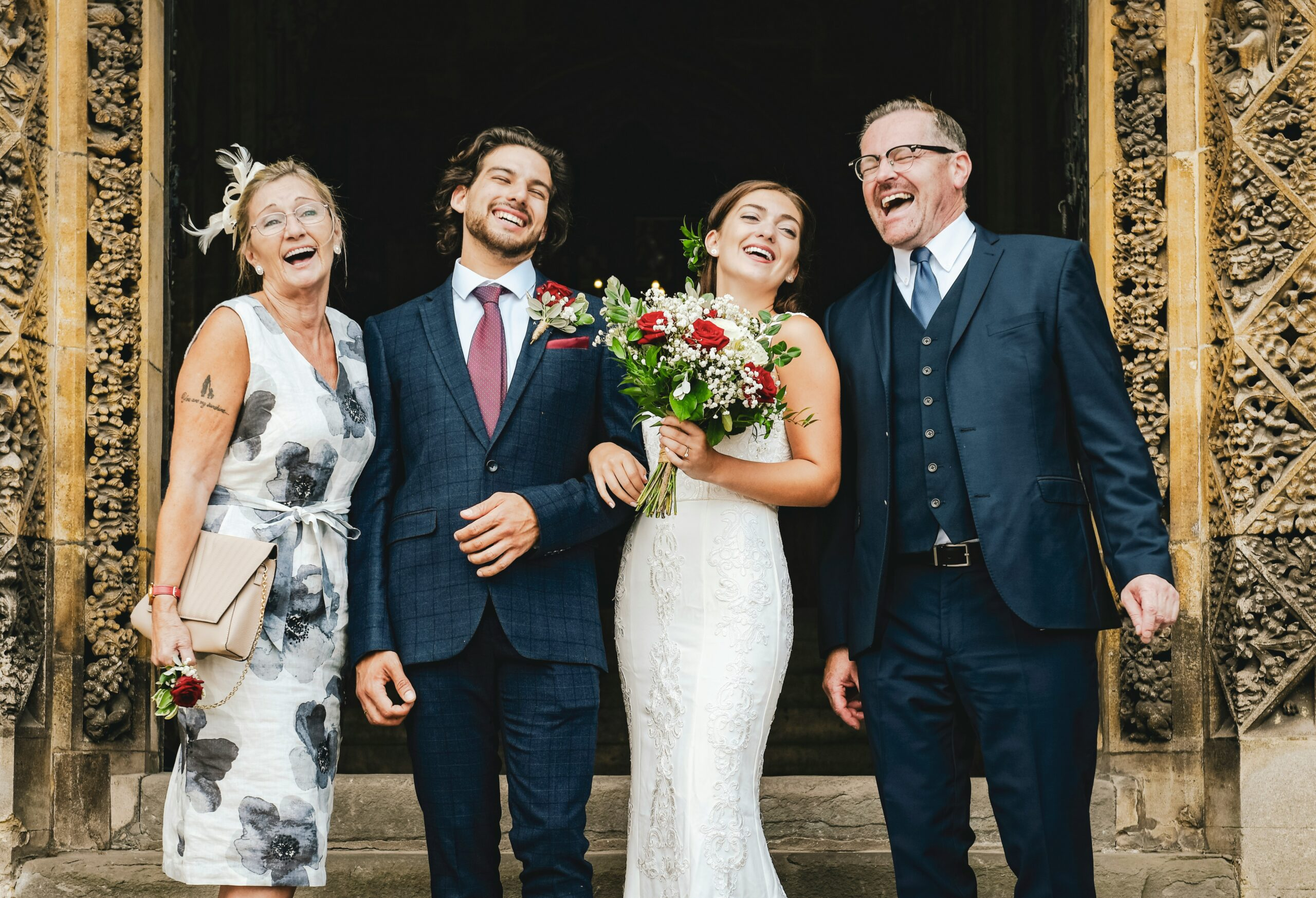 Bride, groom and parents laughing together at a church doorway