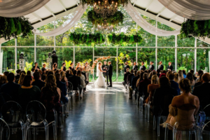 Greenhouse-style wedding ceremony with hanging chandelier and seated guests